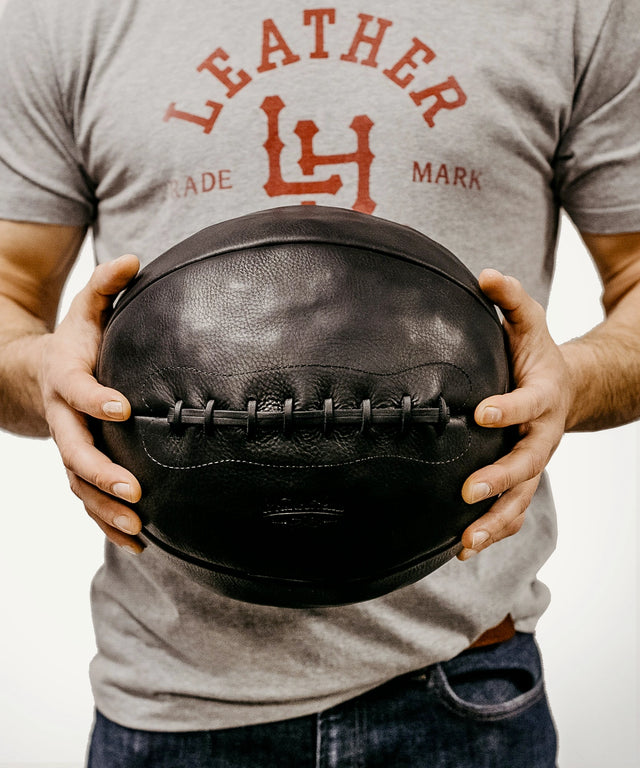 Leather Head Sports 14 lb leather medicine ball held by person wearing gray shirt and jeans