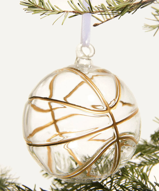Hand-blown glass Christmas ornament designed like a basketball with gold enamel seams, hanging from a white ribbon.