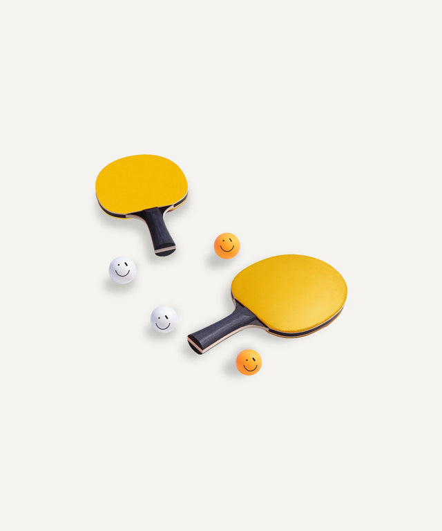 Aesthetic ping pong art featuring two yellow paddles and four smiling table tennis balls on a white background