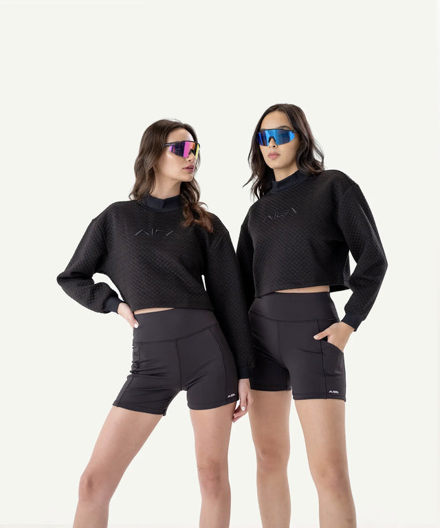 Two women wearing fashionable womens golf clothing by AIEA Golf featuring black quilted crop tops and high-waisted shorts