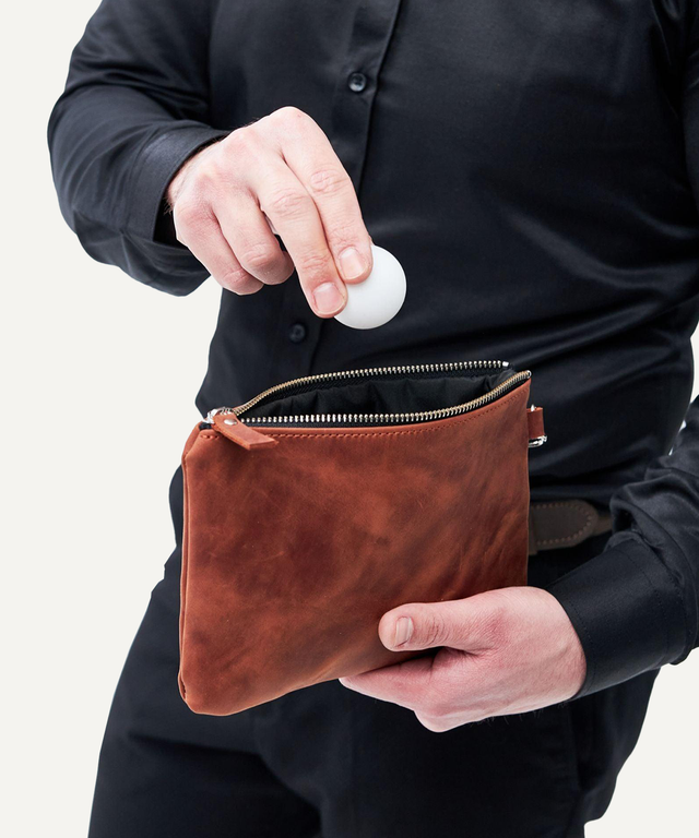 Pikore brown leather golf field pouch held by a man placing a golf ball inside