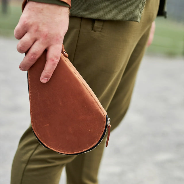 Pikore brown leather ping pong paddle case held by person wearing green pants and jacket