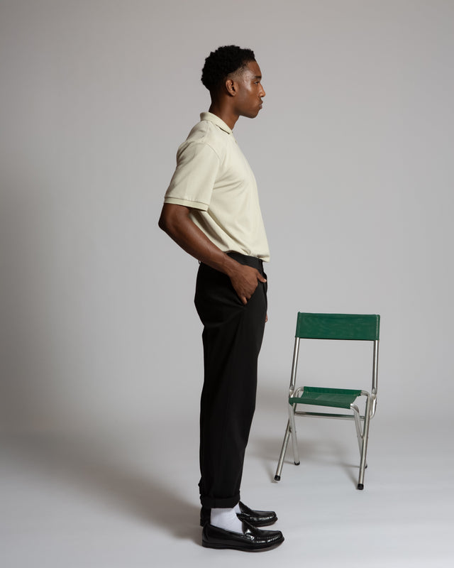 Man wearing Kadet men's performance polo shirt in beige with black pants standing beside green chair