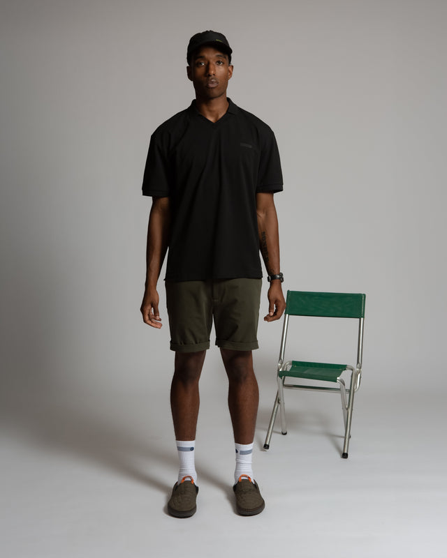 Kadet men's performance polo shirt in black worn with green shorts and a black cap