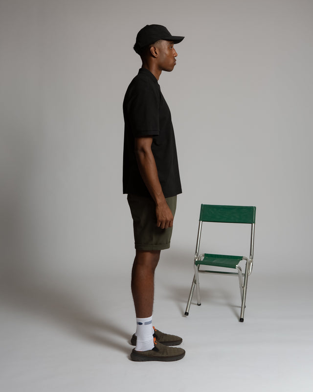 Side view of a man wearing Kadet men's performance polo shirt in black with shorts and cap