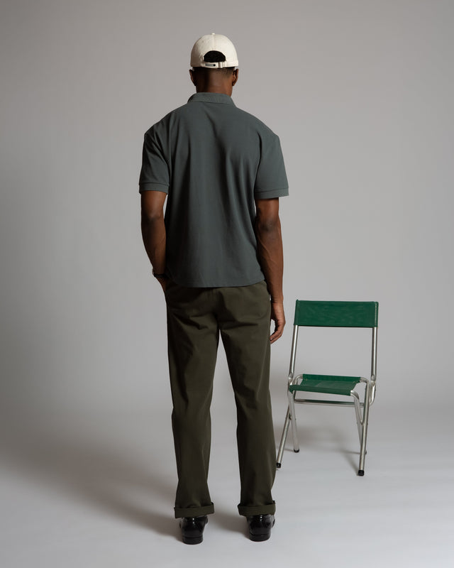 Back view of a man wearing a Kadet men's performance polo shirt in dark gray with olive pants and a white cap