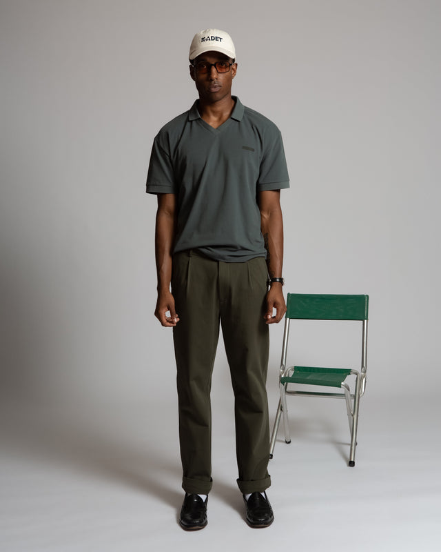 Kadet men's performance polo shirt in dark green worn by male model with cap and glasses