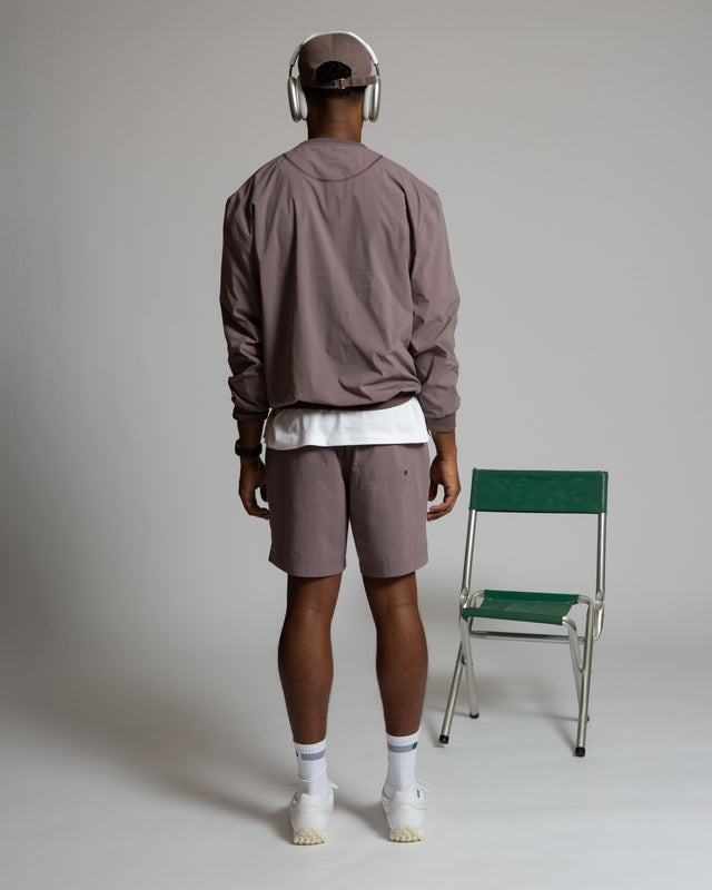 Back view of man wearing Kadet Fabien windbreaker jacket in muted purple with matching shorts and white sneakers