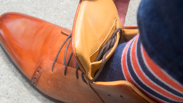 Handcrafted brown premium leather dress shoes being worn with striped socks close-up