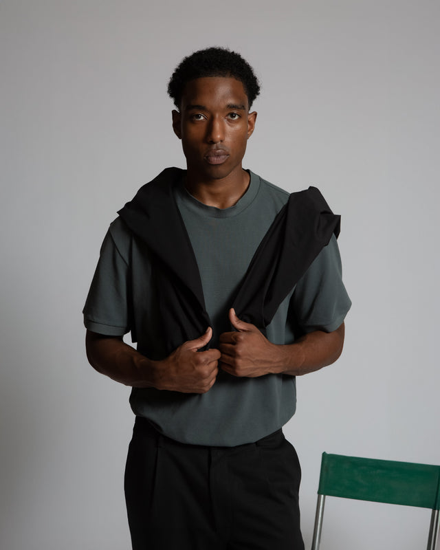 Man wearing Henrik pique tee for men in dark green with black sweater draped over shoulders