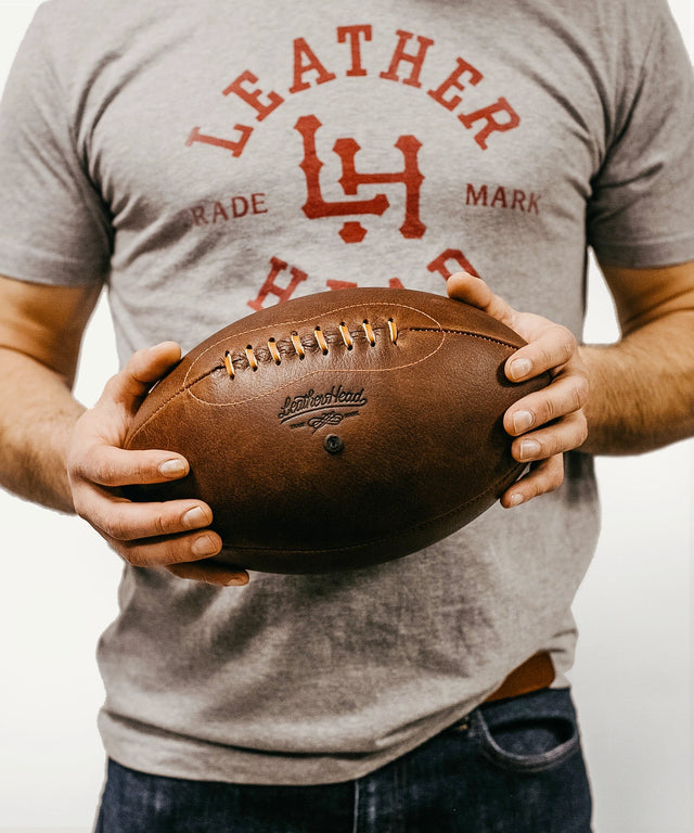 Man holding a premium leather rugby ball by Leather Head Sports wearing a gray Leather Head t-shirt
