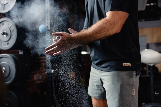 Man wearing Solstice Athletics premium workout clothing chalking hands in gym setting