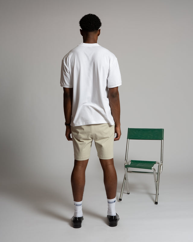 Rear view of man wearing beige men's chino shorts and white t-shirt standing next to green chair