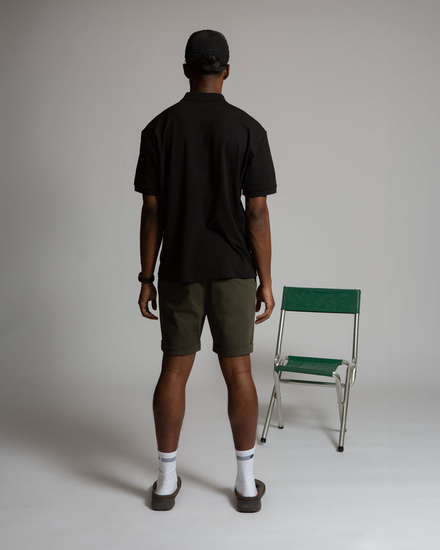 Back view of a man wearing Kadet men's chino shorts in olive green with a black shirt and cap