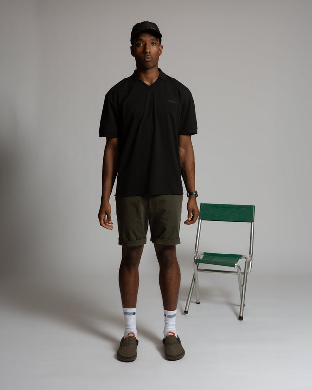 Kadet men's chino shorts in olive green worn with black shirt and cap in studio