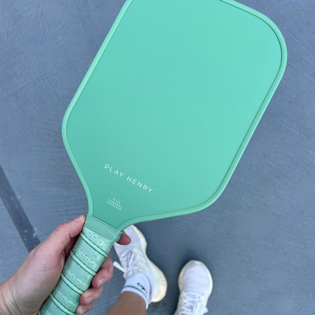 Play Henry carbon fiber pickleball paddle in teal color held in hand on court background