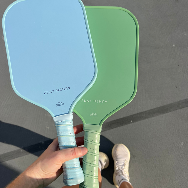 Play Henry carbon fiber pickleball paddle set in blue and green held by hand on outdoor court