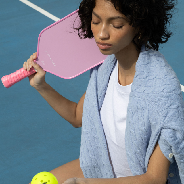 Play Henry pink carbon fiber pickleball paddle held by woman on blue court with yellow pickleball