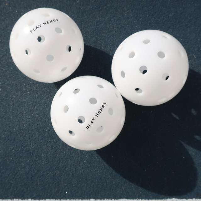 Play Henry white outdoor pickleball balls with ventilation holes on dark blue court surface