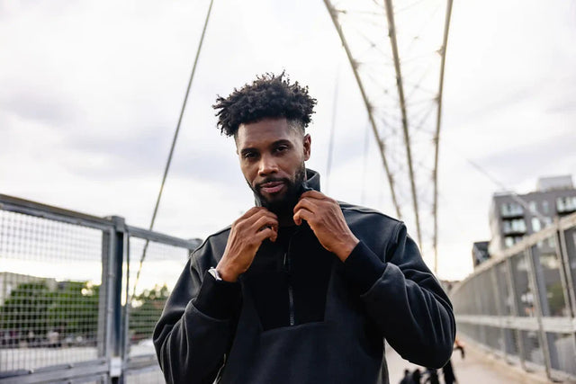 Man wearing Solstice Athletics black jacket showcasing premium workout clothing on urban bridge