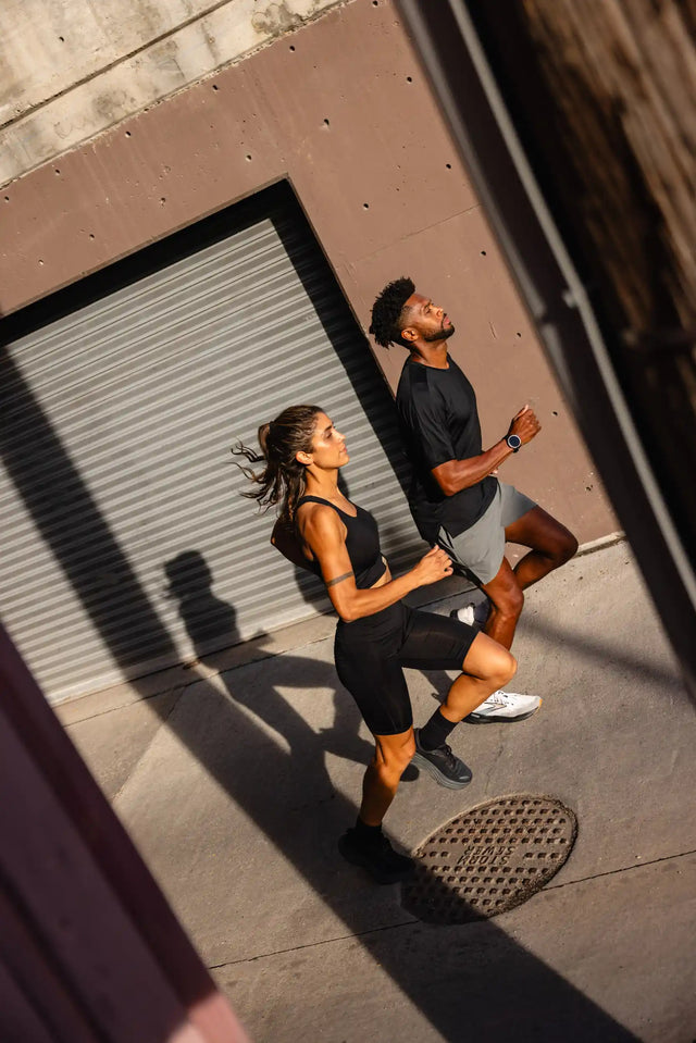 Two athletes wearing Solstice Athletics premium workout clothing exercising outdoors against urban backdrop