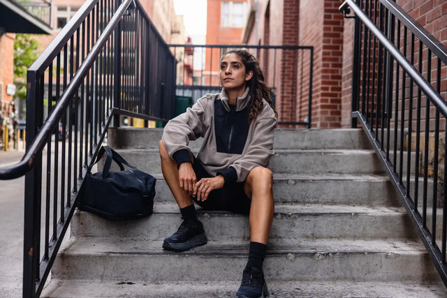 Woman wearing Solstice Athletics premium workout clothing sitting on concrete stairs with black gym bag