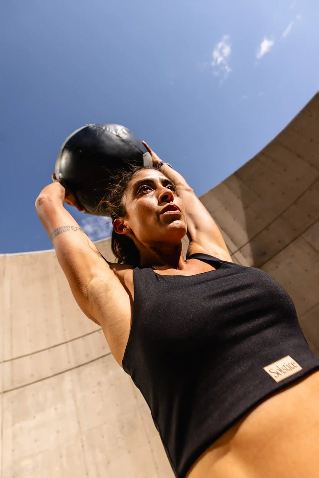 Woman wearing Solstice Athletics premium workout clothing lifting a medicine ball outdoors