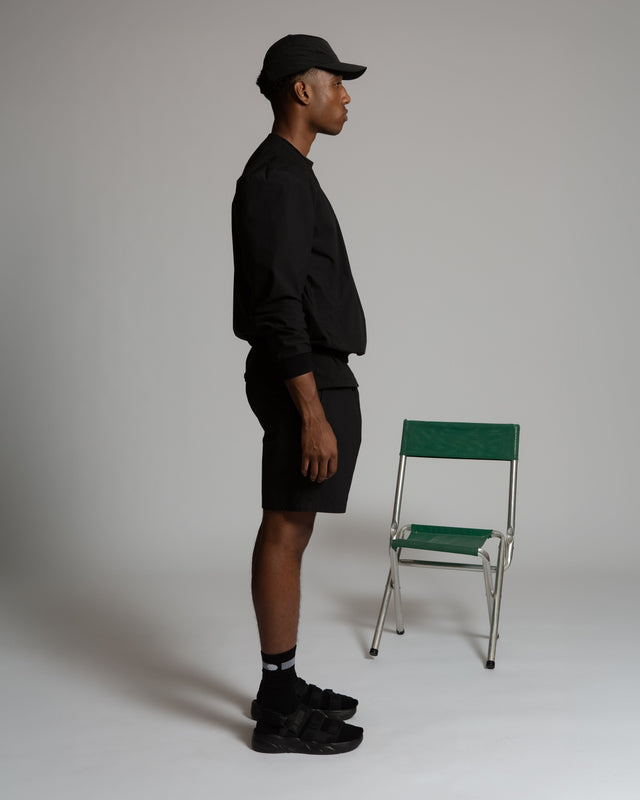 Side view of a man wearing black women's pull-on athletic shorts and matching black cap and sweatshirt