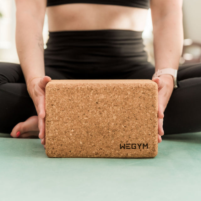 WeGym cork yoga block held by woman sitting on yoga mat for support and balance