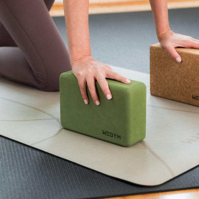 WeGym green and cork foam exercise block used during yoga practice on a beige and black mat